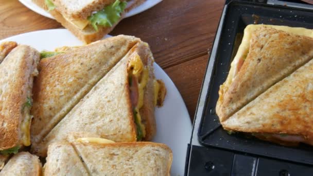 Πρωινό στην κουζίνα του σπιτιού. Σάντουιτς με μπέικον, τυρί τσένταρ και μαρούλι τηγανίζονται σε ειδική τοστιέρα ή τοστιέρα. Ειδική σπάτουλα κουζίνας παίρνει φρέσκο ψωμί σάντουιτς — Αρχείο Βίντεο