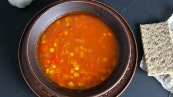 Vista superior sobre sopa vegetariana de tomate vermelho quente com legumes e milho em uma placa vintage de barro em um fundo preto em estilo rústico — Vídeo de Stock