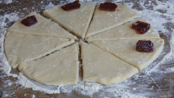 As mãos femininas põem-se com um colher de chá em umas partes de círculo do engarrafamento de cereja na massa de farinha crua de futuros croissants. Doces caseiros. Engarrafamento, a massa, feito pela mão da mulher na cozinha em casa — Vídeo de Stock