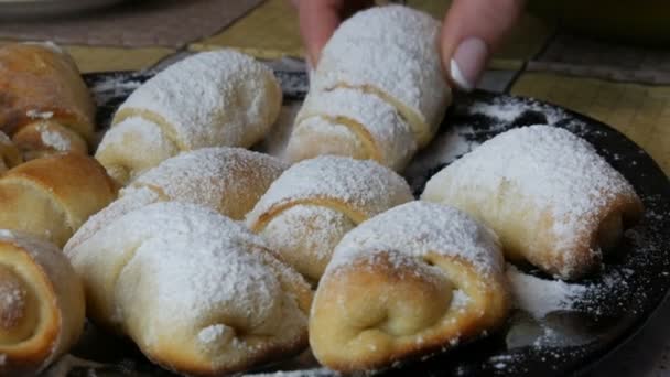 La mano femenina toma croissants caseros recién horneados con azúcar glaseado encima en un plato grande en la cocina — Vídeos de Stock