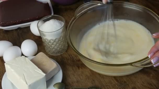 Змішати домашнє тісто для випічки. Жіночі руки змішують з віночком з теплим молоком і яйцем у прозорій тарі. Поруч інгредієнти для майбутніх круасанів. Масло, дріжджі, яйця, цукор і вишневе варення — стокове відео