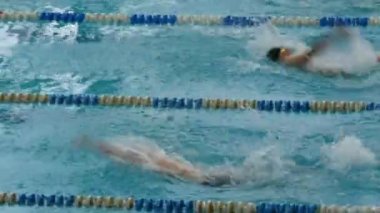 Yüzme eğitiminde yüzen erkekler özel donanımlı büyük bir havuzda dalış gözlüğü ve kepleriyle. Senkronize Sırt Vuruşu