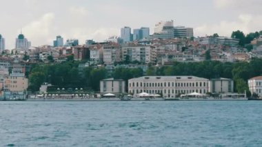 İstanbul, Türkiye - 12 Haziran 2019: Yeşilliklerle çevrili deniz kıyısındaki yeşil tepelerdeki konut binalarının zengin lüks çeyreği. Yoldan geçen bir tekneden görüntü