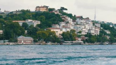 İstanbul, Türkiye - 12 Haziran 2019: Yeşilliklerle çevrili deniz kıyısındaki yeşil tepelerdeki konut binalarının zengin lüks çeyreği. Yoldan geçen bir tekneden görüntü