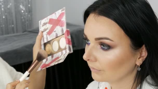20 de septiembre de 2019 - Kamenskoye, Ucrania: Vista de cerca de un artista de maquillaje estilista aplica crema de fundación con un cepillo especial en la cara de una joven hermosa mujer con ojos azules — Vídeo de stock