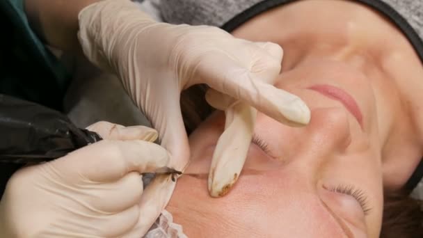 Caneta com uma agulha para maquiagem permanente, as mãos mestras fazem a correção da forma das sobrancelhas no salão de beleza. Método moderno de correção com pulverização em pó. Microblading, tatuagem de sobrancelha — Vídeo de Stock