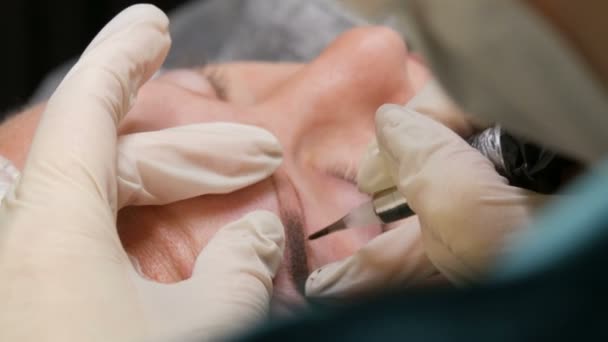 Las manos de un esteticista con guantes blancos aplican pigmento a la piel con la ayuda de una pluma especial. Corrección de forma de ceja. Microblading, maquillaje permanente, maquillaje permanente, pulverización del polvo — Vídeo de stock