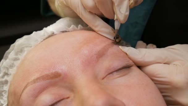 Penna med nål för permanent make-up, gör mästarhänderna korrigering av formen på ögonbrynen i skönhetssalongen. Modern metod för korrigering med pulversprutning. Mikroblads, ögonbrynstatuering — Stockvideo