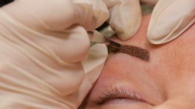 Güzellik salonunun yakın görüntüsünde kaşların şeklini düzeltiyorum. Mikro patlayıcı, kalıcı makyaj, kalıcı makyaj, barut püskürtme.