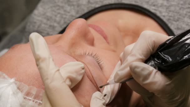 Las manos de un esteticista con guantes blancos aplican pigmento a la piel con la ayuda de una pluma especial. Corrección de forma de ceja. Microblading, maquillaje permanente, maquillaje permanente, pulverización del polvo — Vídeos de Stock