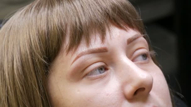 Mujer joven en un estudio de belleza después del procedimiento de corrección de cejas. Nueva forma de ceja. Microblading, tatuajes, maquillaje permanente, pulverización en polvo. Nuevas tecnologías en cosmetología — Vídeos de Stock
