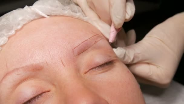 O esteticista corrige as sobrancelhas ao paciente. Marcando o contorno das sobrancelhas com lápis especial — Vídeo de Stock