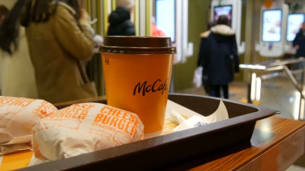 Wien, Österrike - 19 december 2019: Ett glas lattkaffe och ett par ostburgare på en bricka i McDonaldwe mot bakgrund av digitala skärmar för beställningar utan kassaskåp — Stockvideo