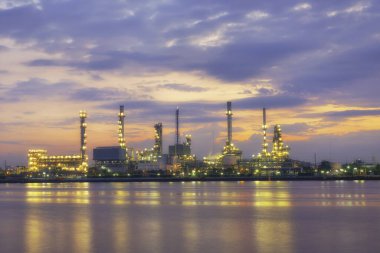 Damıtma tesisi / Petrol rafinerisi ya da petrol rafinerisi tarafından nehrin yanında gün batımı veya gün doğumuyla yansıtılan lamba ışığı.