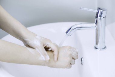 Waoman ellerini lavaboda musluk suyunun altında sabun köpüğüyle yıkıyor ya da temizliyor. İyi hijyen ve koronavirüs koruması kavramı