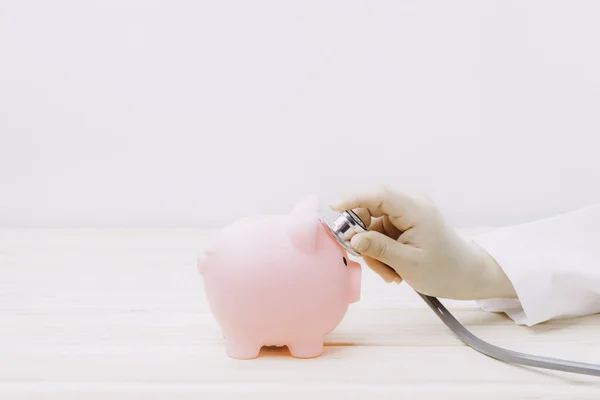 Doctor using stethoscope to check pink piggy bank. Concept check saving money and financial sustainability