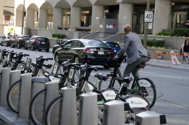 Shared bikes are lined up in the streets. One man wearing suite is using it while bicycles in bike dock  clipart