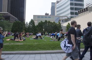  Bir grup kadın practing Yoga yaz aylarında kaldırımda yürüyen insanlar ile şehrin merkezinde yeşil bir alanda bir sınıfta