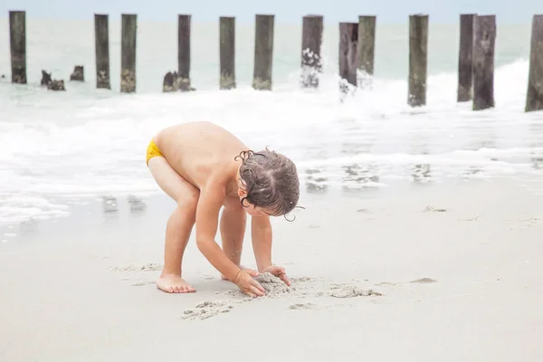 幸せな少年はビーチで砂と遊んでいる 子供たちは海で遊んだり泳いだりします 休暇だ ビーチで子供のための活動 喜びと幸せ — ストック写真