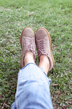 Woman is resting in a park on nature sitting on the grass. Modern stylish creeper shoes. Hipsetrs style. The concentration of relaxation and lifestyle. clipart