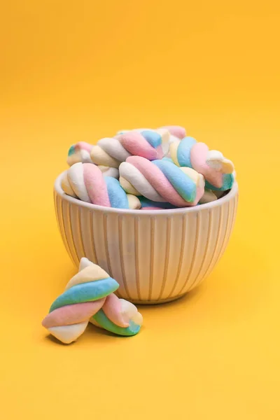 Beautiful cup full of colored marshmallows candies on a yellow background. Concept of sweet food and desserts.