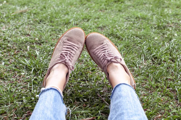 Woman is resting in a park on nature sitting on the grass. Modern stylish creeper shoes. Hipsetrs style. The concentration of relaxation and lifestyle.