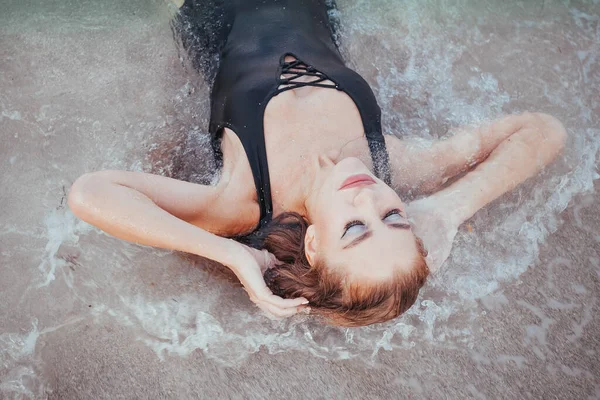 Girl in a wet dress posing in the water. Evening photo shoot for a beautiful blonde with long hair in a gray dress. Walk along the beach at sunset. Vacation and Travel Concept.