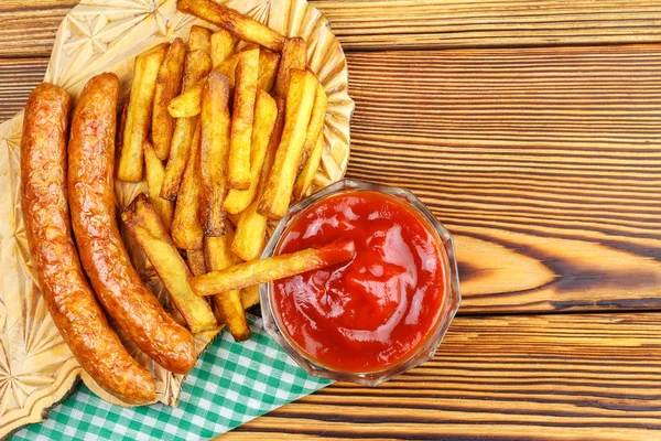 Homemade fast food, portion of french fries, ketchup, grilled sausages on wooden board. — Stock Photo, Image