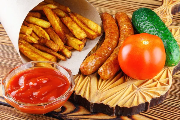 Hemmagjord snabbmat, del av pommes frites, ketchup, grillad korv, tomat, gurka på träskiva. — Stockfoto