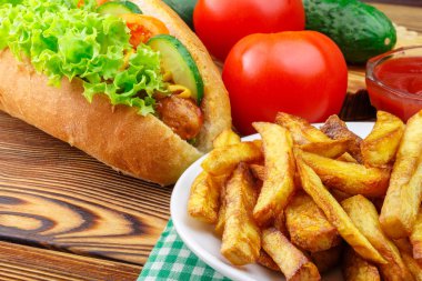 Fast food yemek, sosis, patates kızartması, ketçap, domates ve salatalık ahşap arka plan üzerinde.