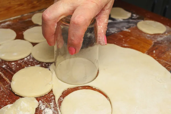 Женщина делает украинские пельмени или вареники, разрезая стаканом круглые куски теста — стоковое фото