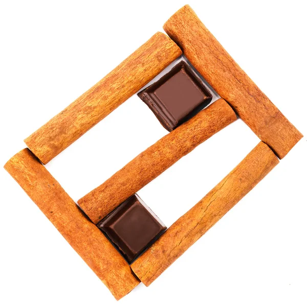 Dark chocolate cubes and cinnamon sticks isolated on white background, top view. — Stock Photo, Image