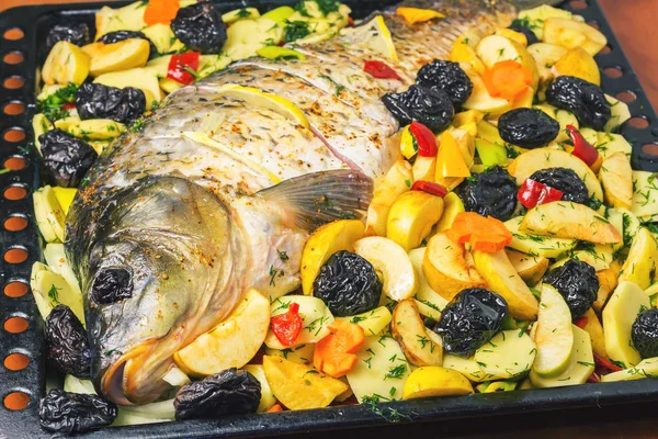 Carp fish prepared for cooking in baking dish with vegetables.