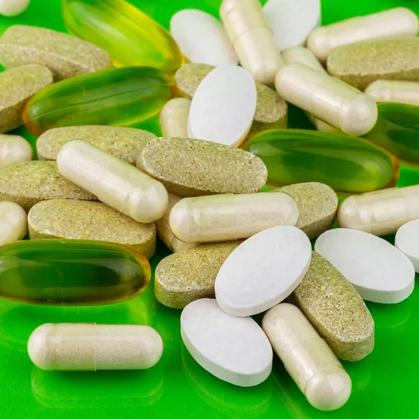 Mixed natural food supplement pills, omega 3, calcium, multivitamin and glucosamine capsules on green background. — Stock Photo, Image