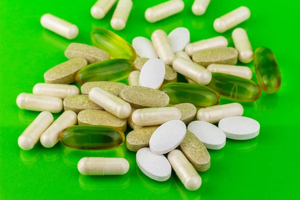 Vegyes természetes étrend-kiegészítő tabletták, omega-3, kalcium-, glükózamin és a multivitamin kapszula-zöld háttér. — Stock Fotó