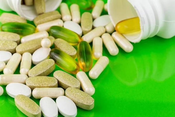 Píldoras de suplementos alimenticios naturales mixtos, omega 3, calcio, multivitaminas y glucosamina cápsulas sobre fondo verde . — Foto de Stock