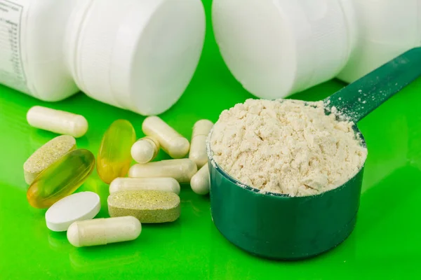 Mixed natural food supplement pills and protein powder in plastic spoon on green background. — Stock Photo, Image