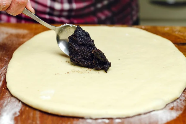 Процес приготування штрудель пирога, жіноча ложка кладе макову начинку на тісто, дерев'яна дошка . — стокове фото