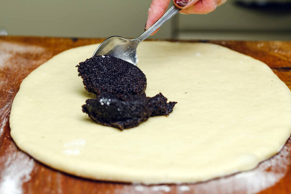 Process of making strudel pie, woman spoon puts poppy stuffing on the dough, wooden board.
