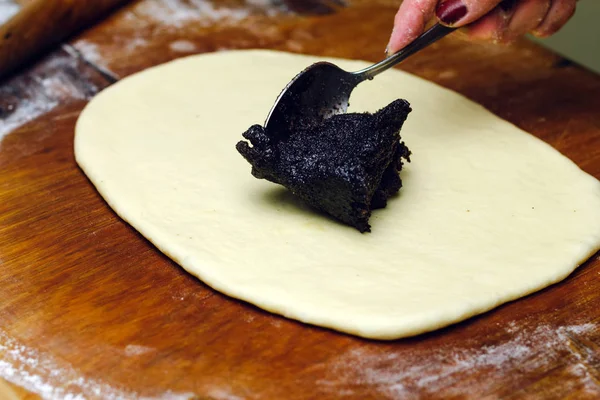Processus de fabrication de tarte strudel, femme cuillère met la farce de pavot sur la pâte, planche en bois . — Photo