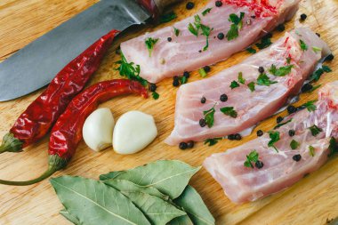 Ahşap tahta üzerinde kırmızı Şili biber, defne yaprağı, sarımsak, baharat ve bıçak ile gümüş sazan balığı pişmiş parçaları