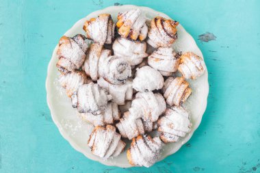 Ev yapımı taze kurabiye silkeledi şekere de beyaz plaka üzerinde ahşap mavi arka plan, üstten görünüm.