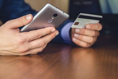 Resmi aşınma, akıllı telefon kullanan ve online alışveriş ve ödeme için kredi kartı tutan erkek elleri, seçici odaklanma