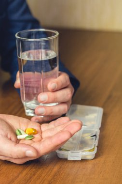 Bir bardak su, vitamin ve besin takviyesi hapları iş adamının iş yerinde elinde, yakın plan.