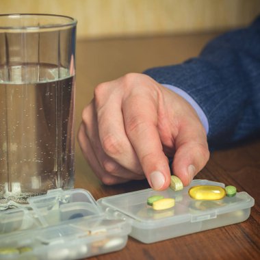 Bir bardak su, vitamin ve besin takviyesi hapları iş adamının iş yerinde elinde, yakın plan.