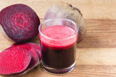 Bardakta taze pancar suyu ve tahta masada dilimlenmiş pancar kökü.