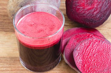 Bardakta taze pancar suyu ve tahta masada dilimlenmiş pancar kökü.