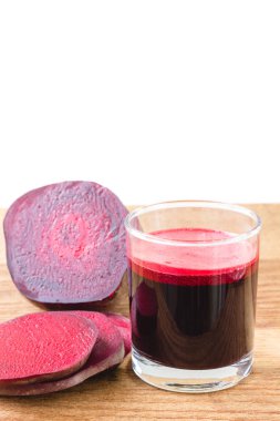 Bardakta taze pancar suyu ve tahta masada dilimlenmiş pancar kökü, beyaz arka plan.