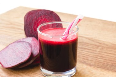 Bardakta taze pancar suyu ve tahta masada dilimlenmiş pancar kökü, beyaz arka plan.