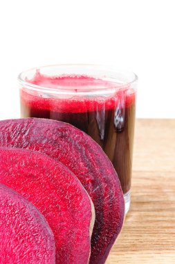 Bardakta taze pancar suyu ve tahta masada dilimlenmiş pancar suyu, beyaz arka plan.